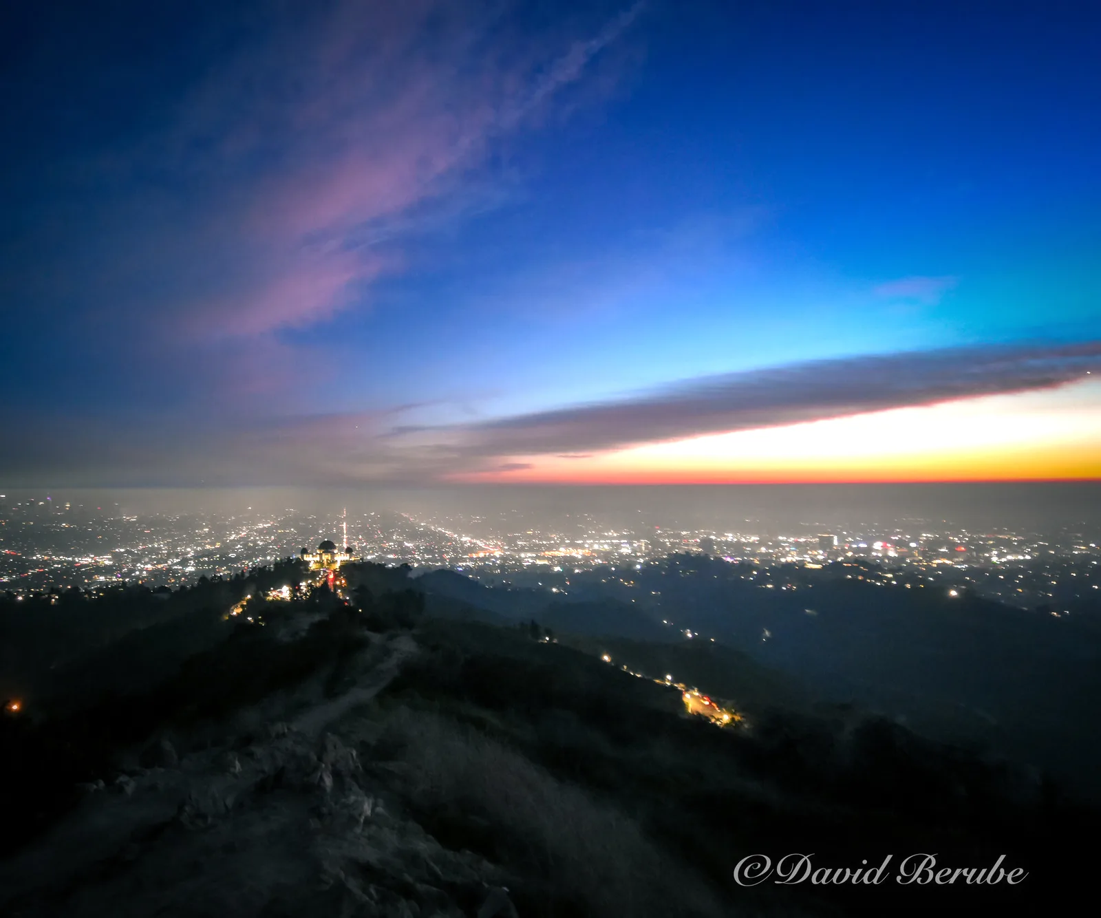 A city at dusk seen from a ridge, with the city lights glowing softly.