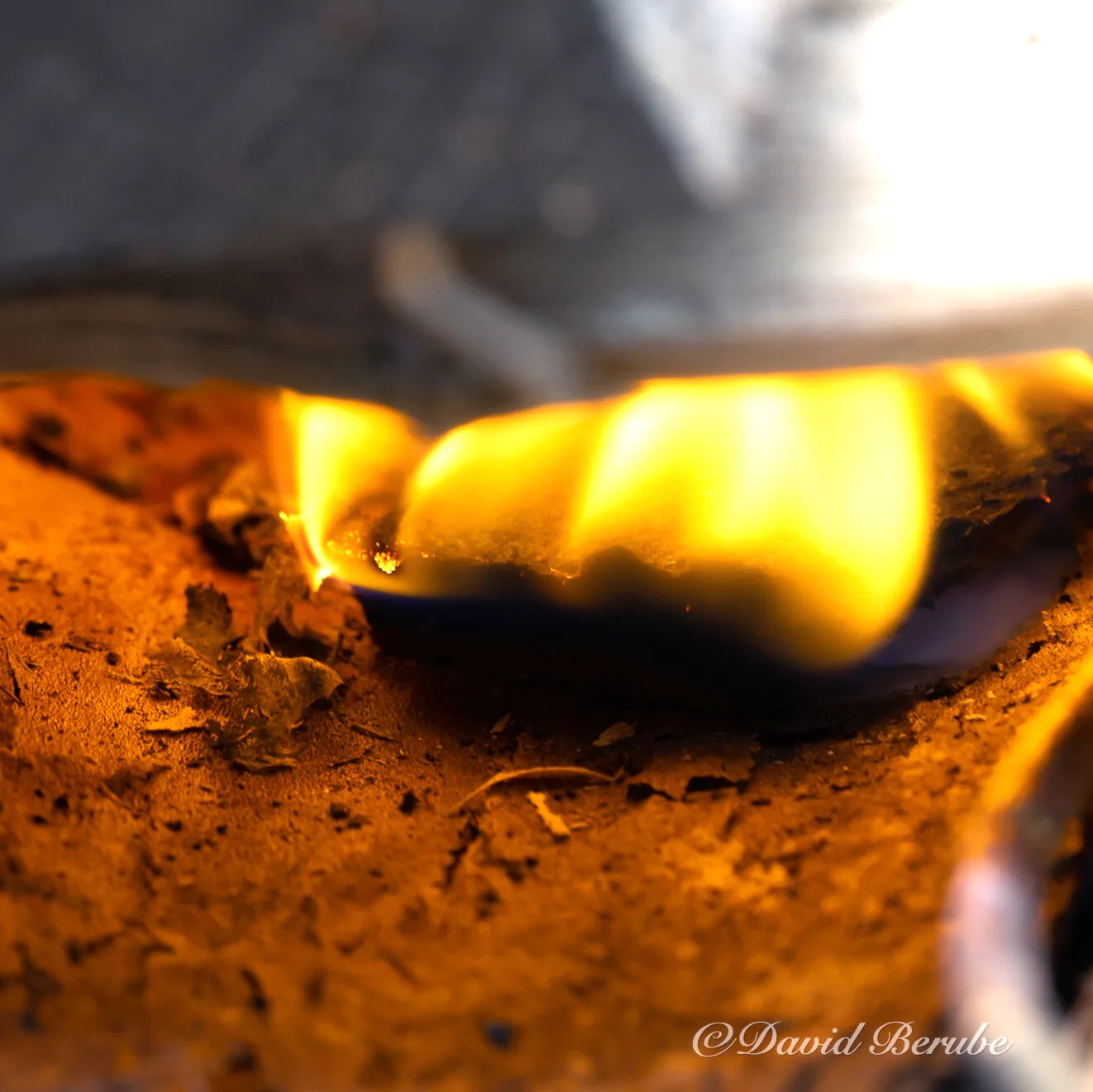 A close-up of a small flame on dirt, glowing.