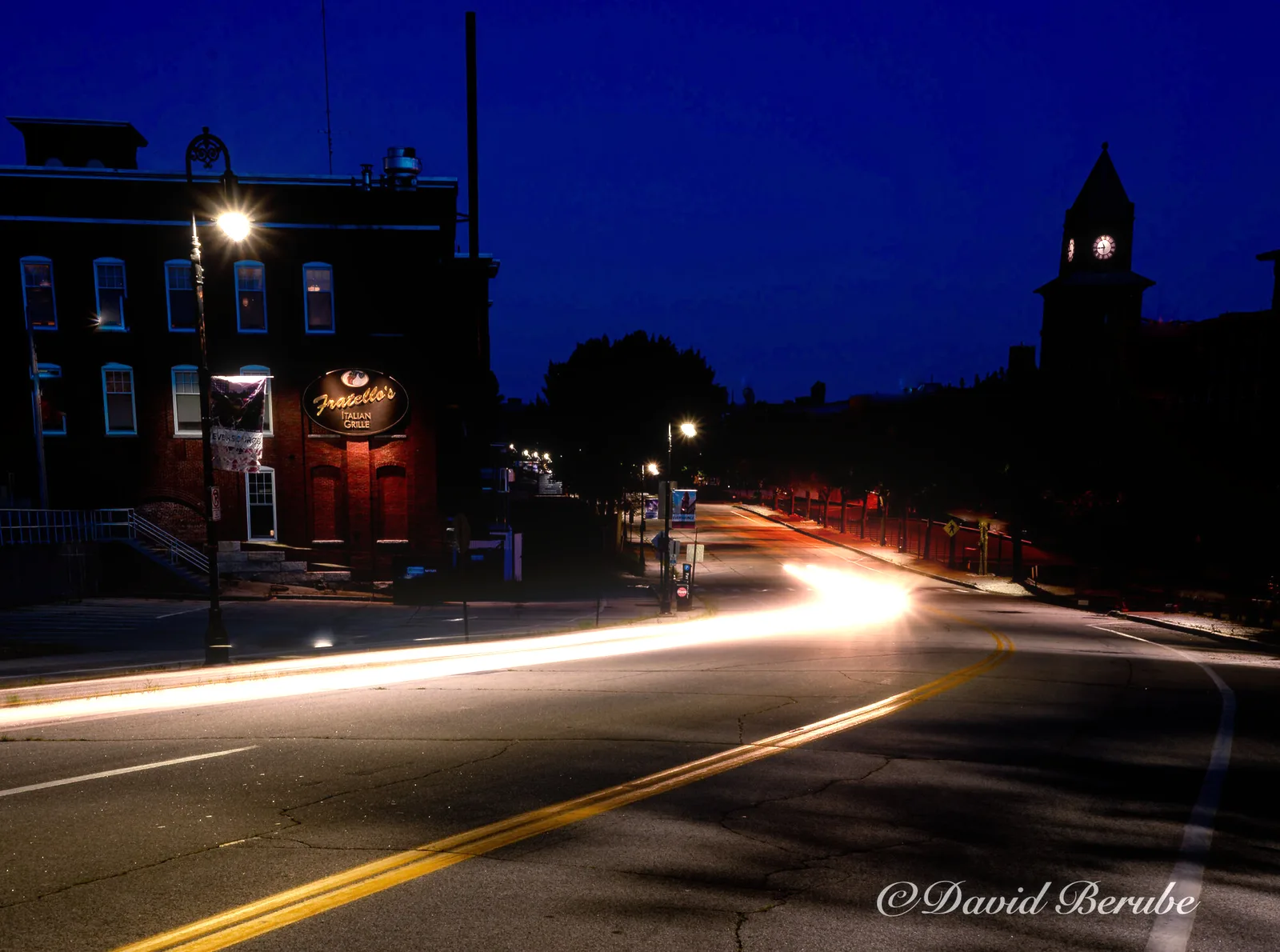 A small-town street at night with streetlamps and car light trails, with bloom, veil, corona and six-blade streaks added.