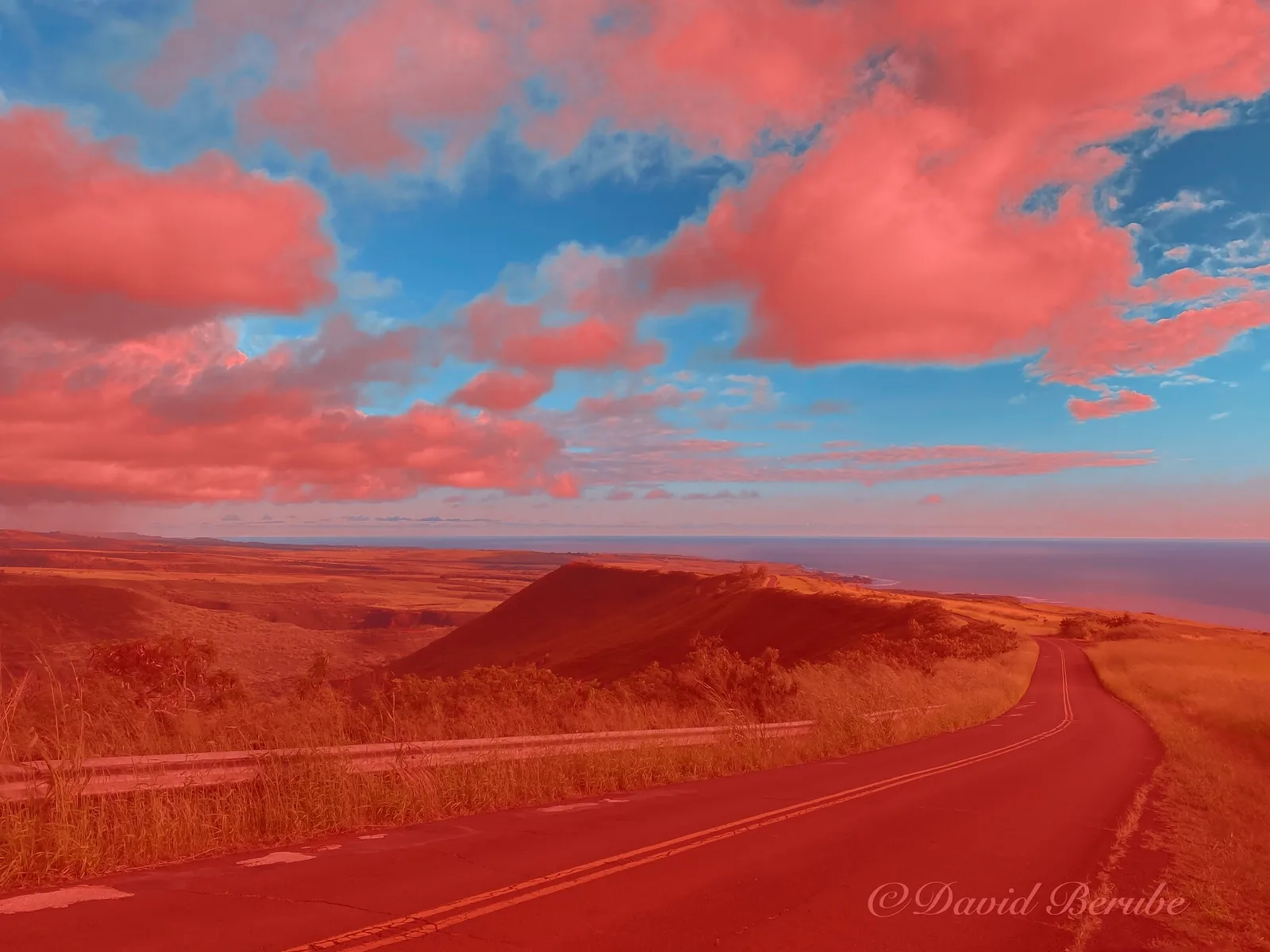 A coastal road under a cloudy sky, with everything but the blue sky tinted red to show the mask.